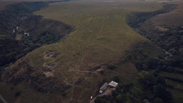 Foto des Geländes von Dmanisis Gora in der Abenddämmerung, das das Plateau zwischen den zwei Schluchten zeigt. Im Vordergrund sind Ausgrabungen der inneren Festung aus dem Jahr 2023 zu sehen.