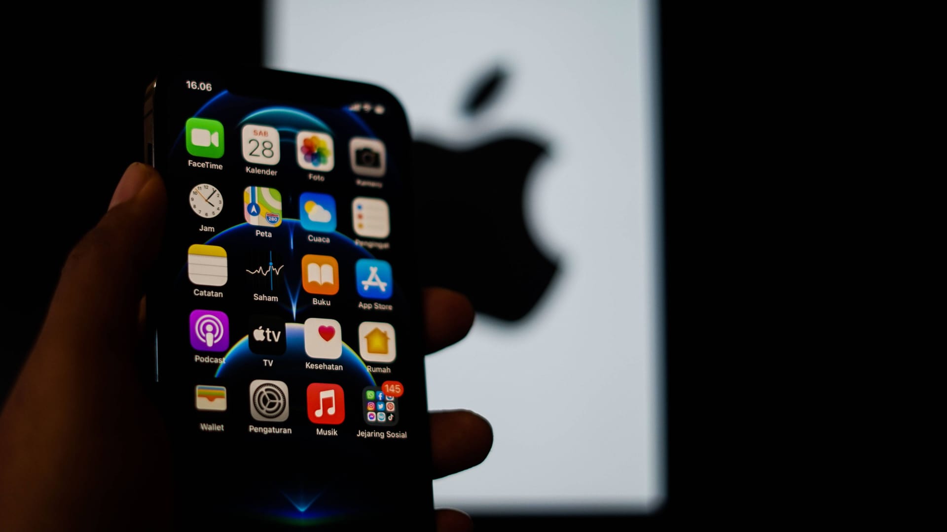 Jemand hält ein iPhone in der Hand und im Hintergrund ist das Apple-Logo. Jemand hält ein iPhone in der Hand und im Hintergrund ist das Apple-Logo.