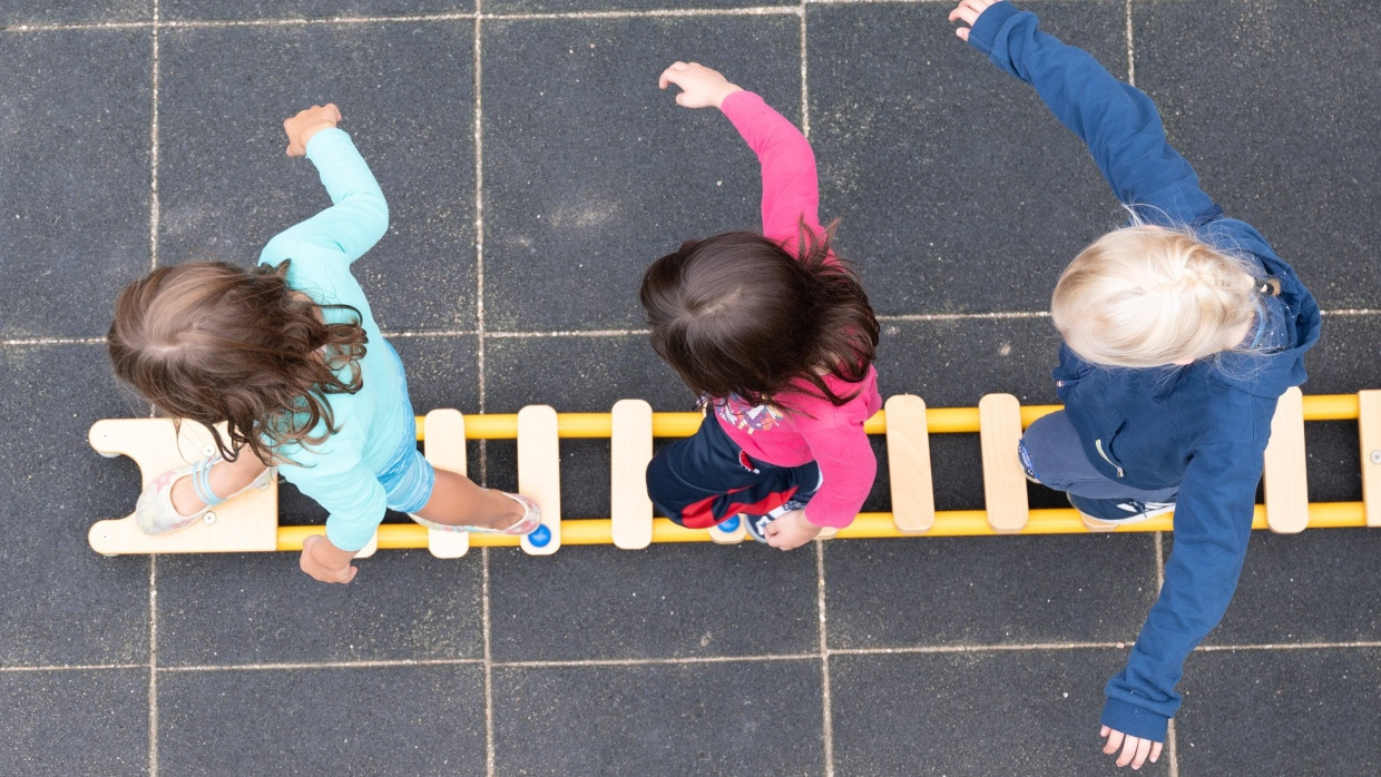 Kinder balancieren in Sachsen auf dem Spielplatz einer Kindertagesstätte auf einem Brett.