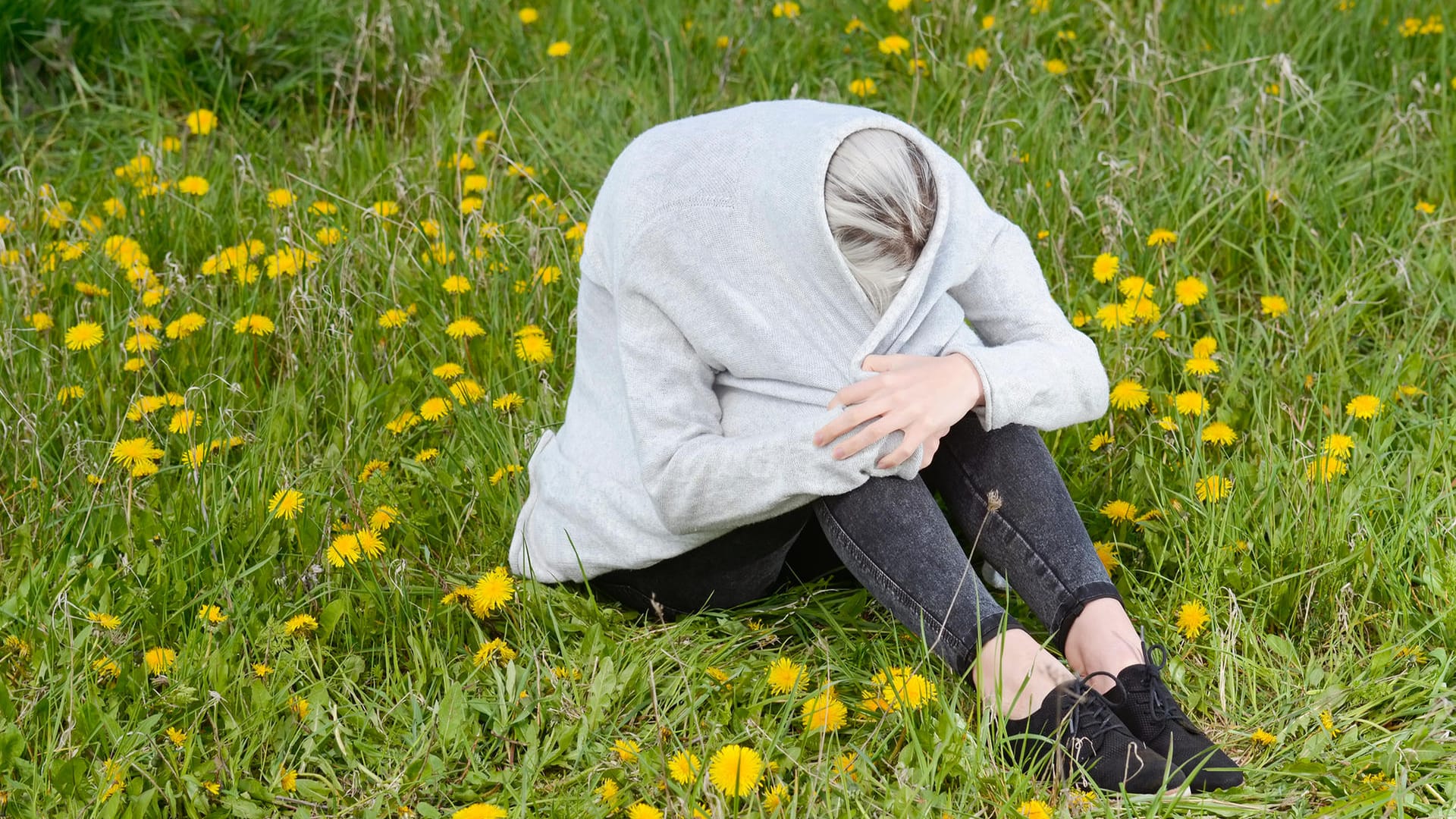 Frau sitzt in Jacke eingewickelt auf einer Wiese Frau sitzt in Jacke eingewickelt auf einer Wiese