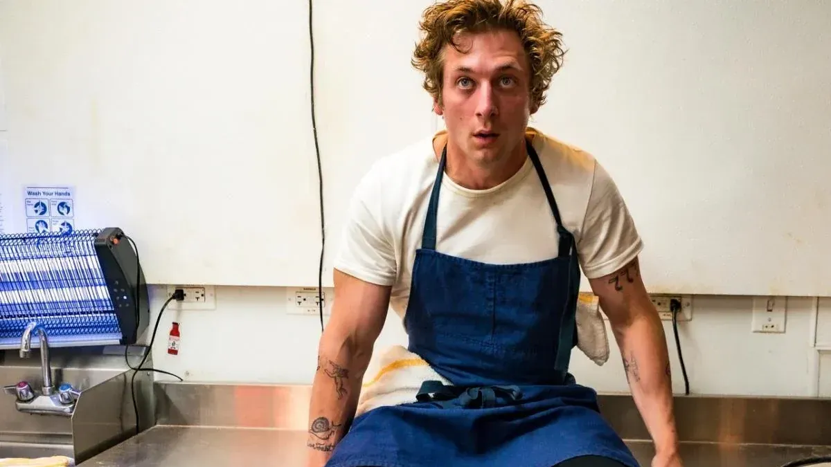 Szenenfoto aus der Serie "The Bear". Schauspieler Jeremy Allen White sitzt auf einem Tisch. Szenenfoto aus der Serie "The Bear". Schauspieler Jeremy Allen White sitzt auf einem Tisch.