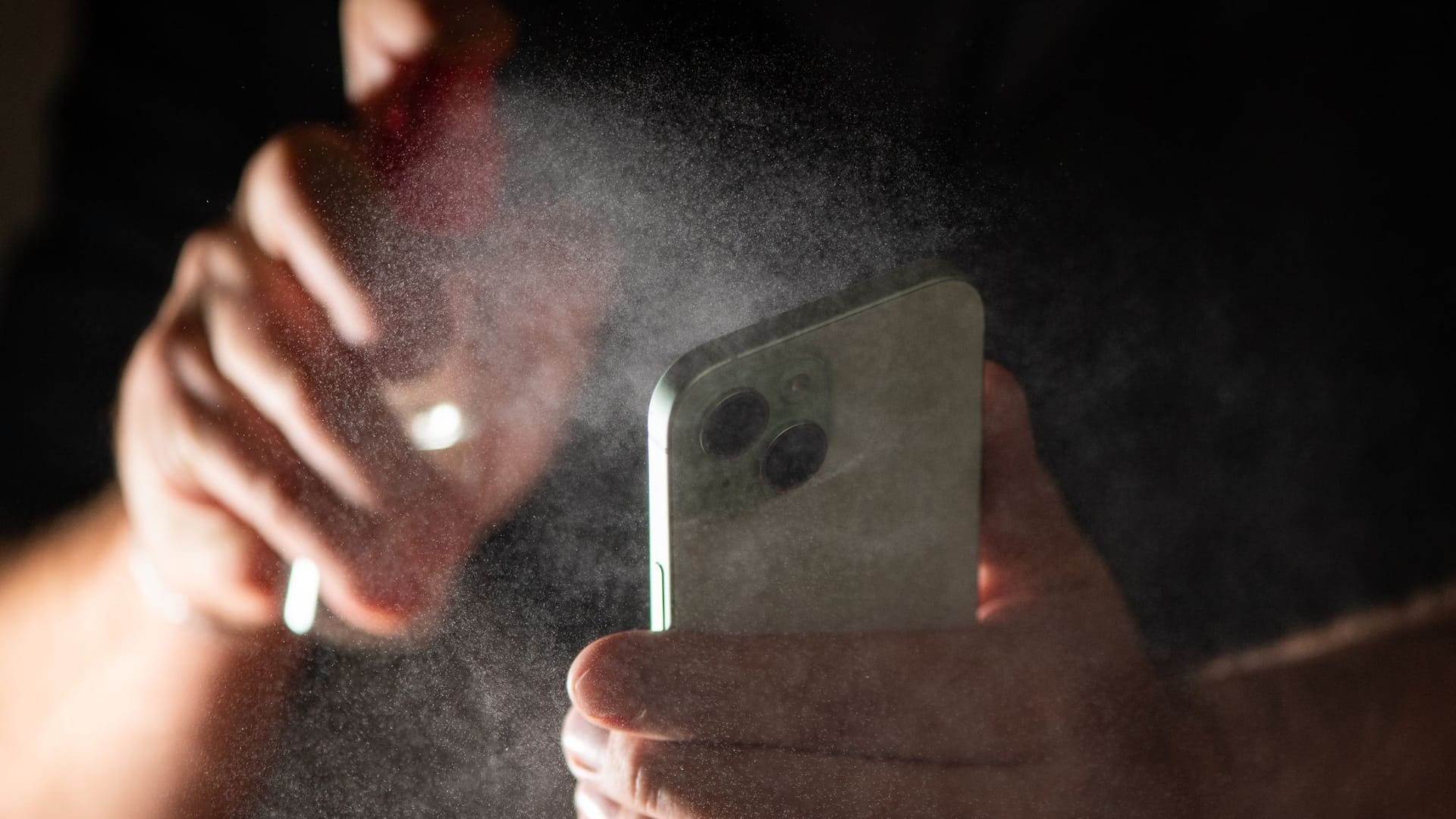 Mann reinigt sein Smartphone mit einem Spray