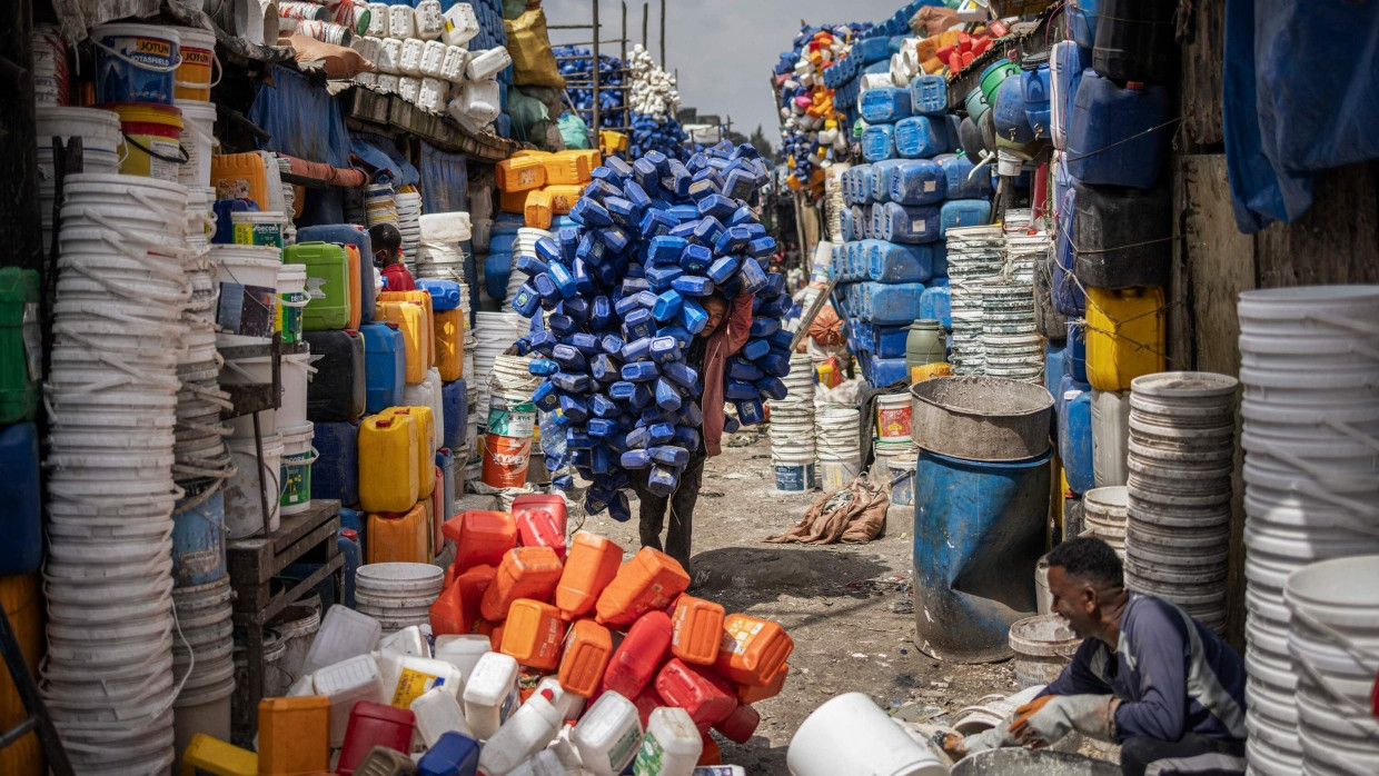 Ein Mann bewegt einen riesigen Stapel von Plastik-Seifenbehältern, während Händler und Käufer zwischen Bergen von Plastik im historischen Merkato-Viertel von Addis Abeba am 1. Oktober 2024 Handel treiben.